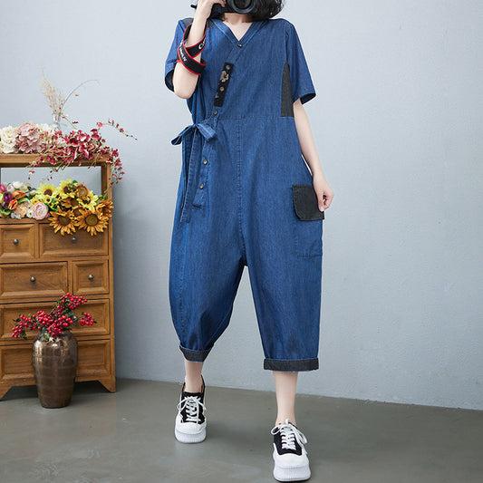 Person wearing a blue denim jumpsuit standing in front of a wooden cabinet with flowers.