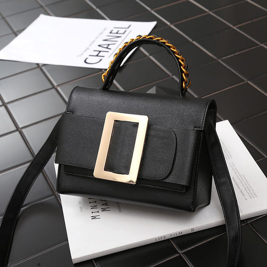Black handbag with gold buckle on a gray surface with Chanel paper.