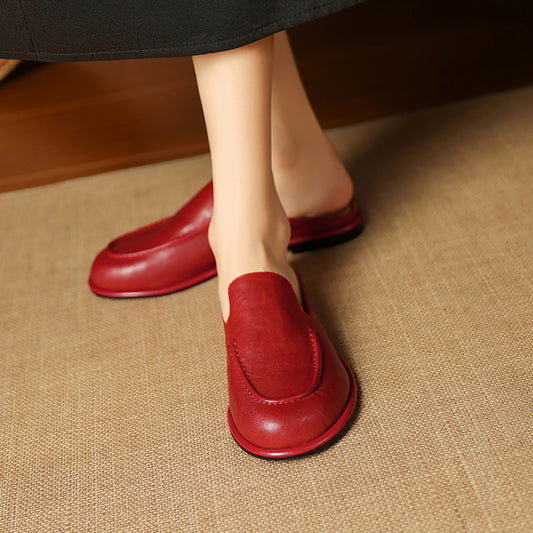 Red loafers worn on a person's feet on a textured surface