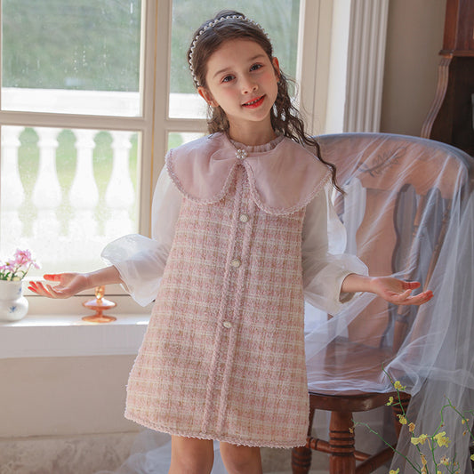 Young girl in a checkered dress standing in a room with a window and chair.