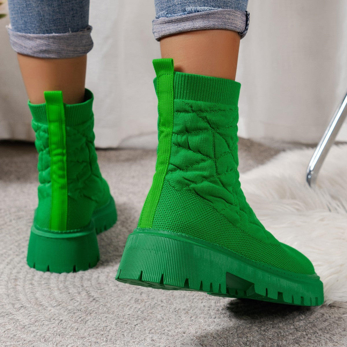 Green chunky boots worn with rolled-up jeans on a neutral background
