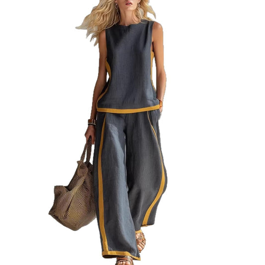 Woman wearing a gray sleeveless top and wide-leg pants with yellow trim, holding a brown bag on a white background.