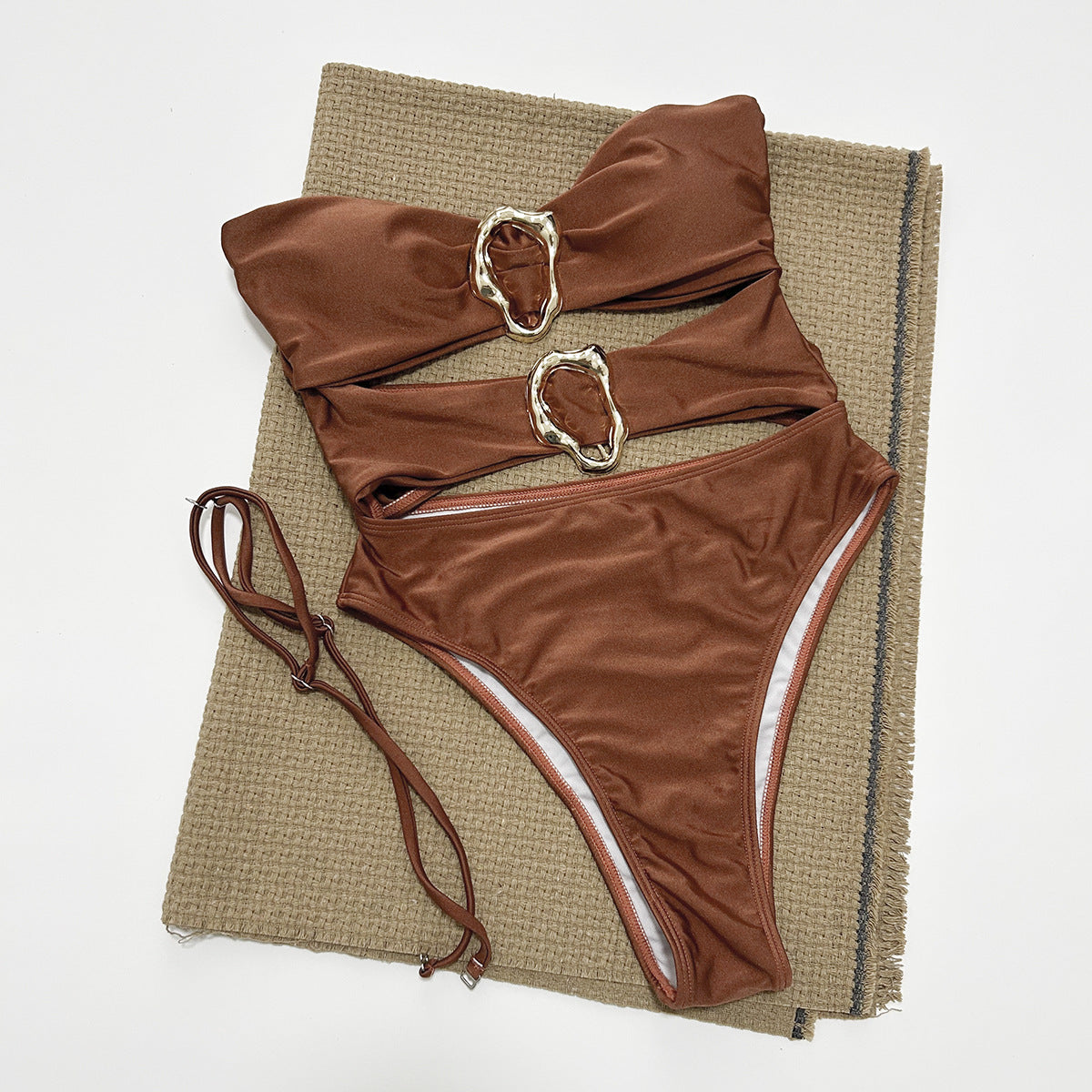 Brown bikini set with metallic buckles on a textured mat