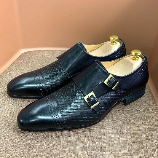 Pair of black leather shoes with gold buckles on a textured surface.