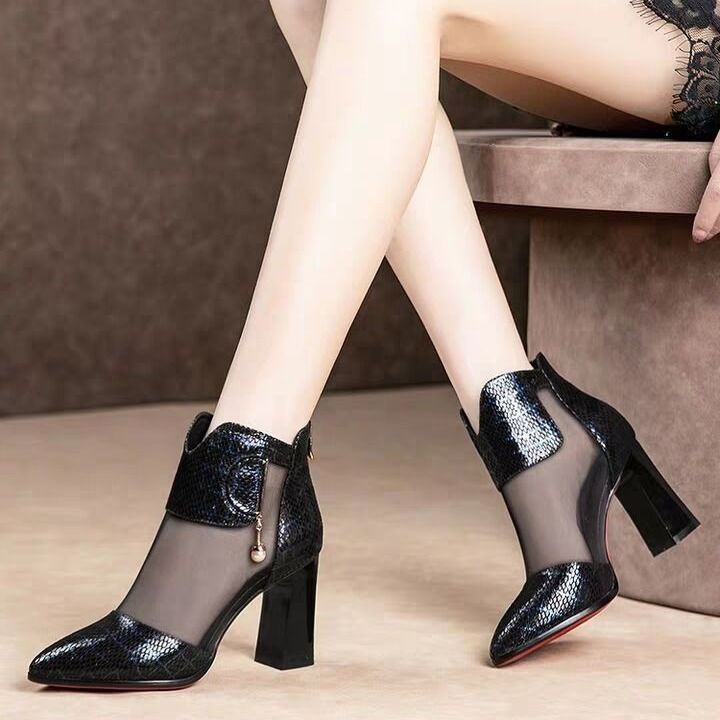 Black high-heeled shoes with sheer mesh design worn by a person sitting on a chair.