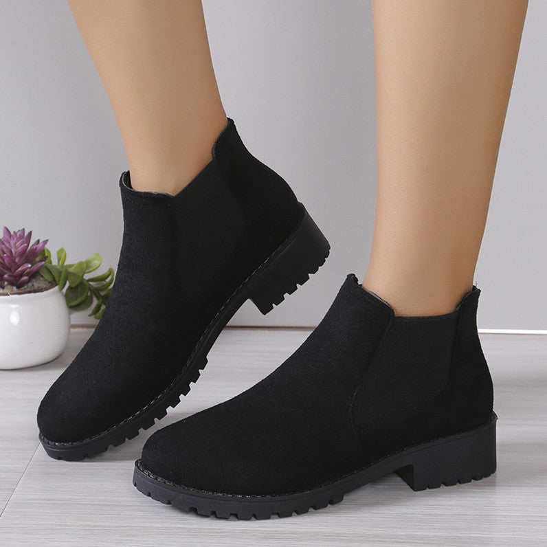 Black ankle boots worn by a person on a light wooden floor with a neutral background