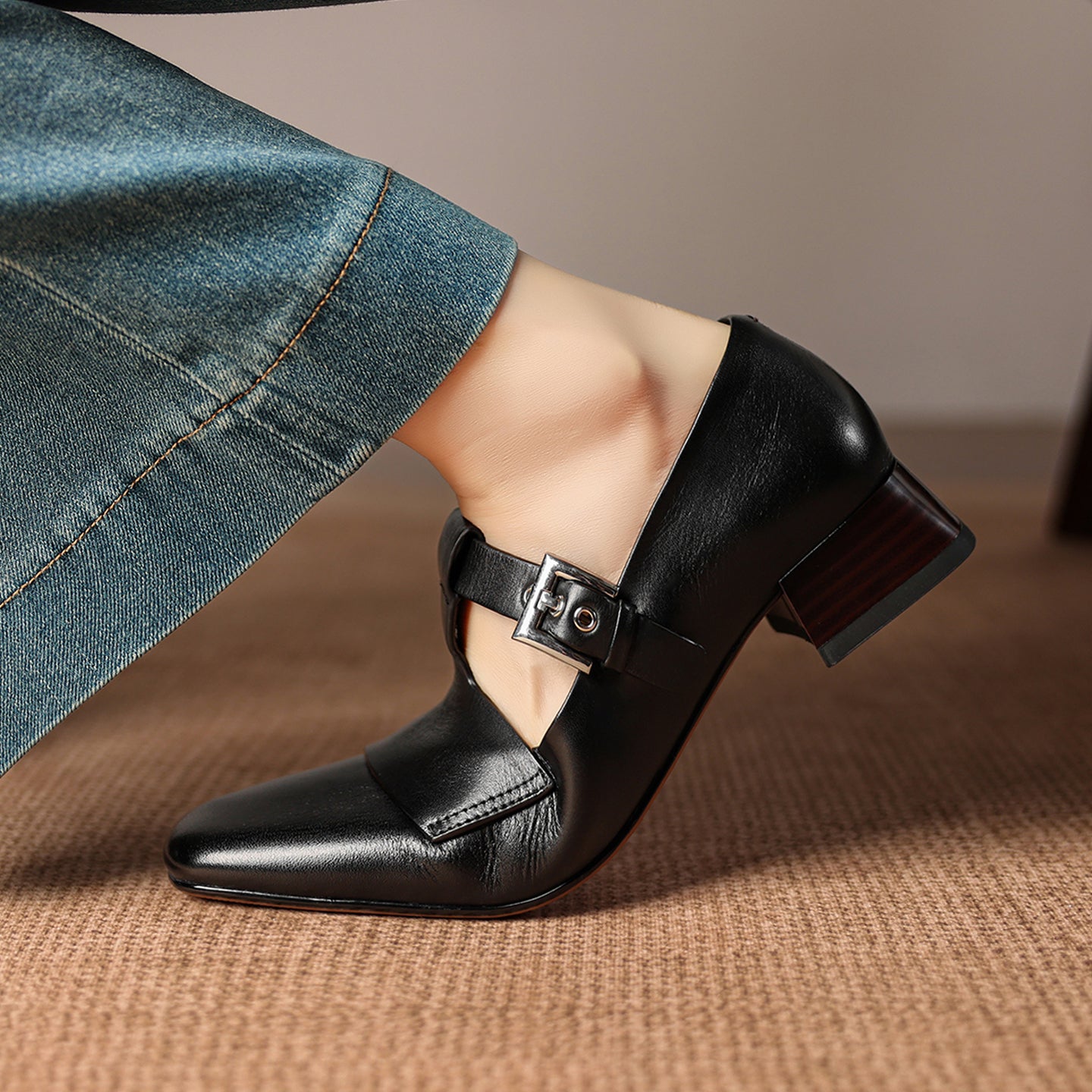 Black leather shoe with a buckle on a brown surface