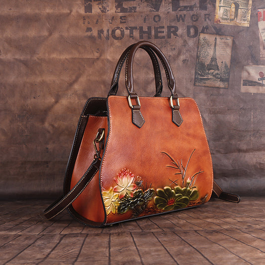 Brown leather handbag with floral design on a wooden floor against a textured wall.