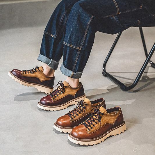 Brown leather shoes worn with rolled-up jeans on a concrete floor.