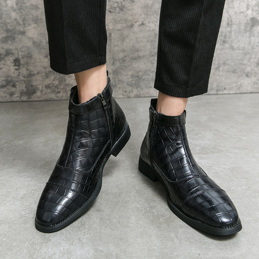 Black crocodile-patterned boots worn with black pants on a gray concrete floor.