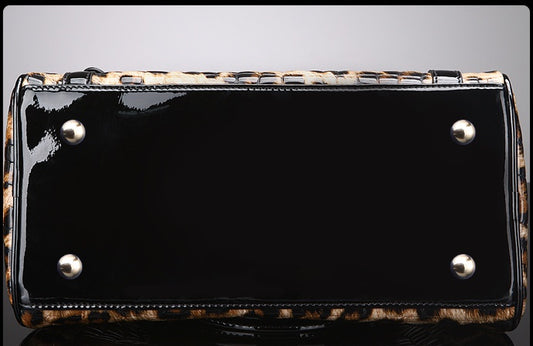 Black patent leather handbag with leopard print trim on a gray background
