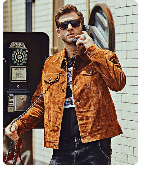 Man in a brown suede jacket using a payphone outdoors.