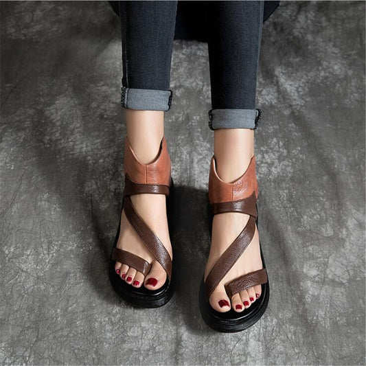 Brown strappy sandals worn with dark jeans on a gray surface