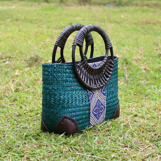 Woven handbag with decorative handles on grass