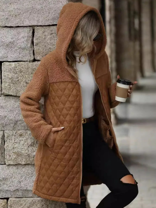 Person wearing a brown quilted coat holding a coffee cup against a stone wall.