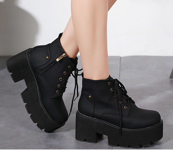 Black platform boots with gold accents worn by a person on a gray surface.
