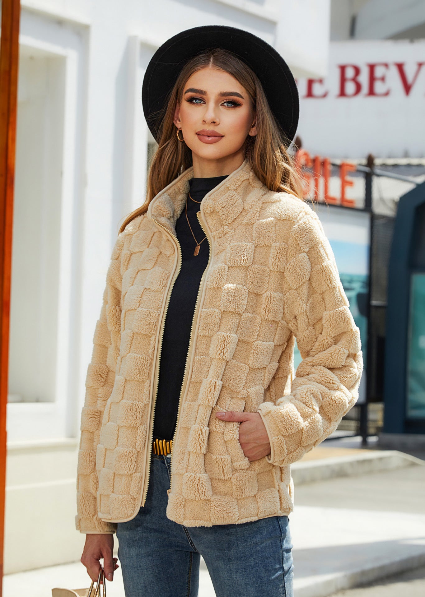 Woman wearing a beige textured jacket and black hat outdoors.
