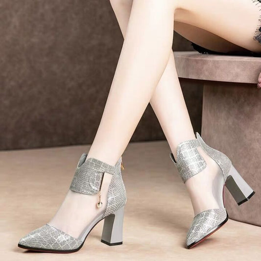 Silver high-heeled shoes worn by a person sitting on a beige surface.