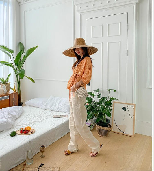 Woman in a stylish outfit standing in a bedroom with plants and decor.