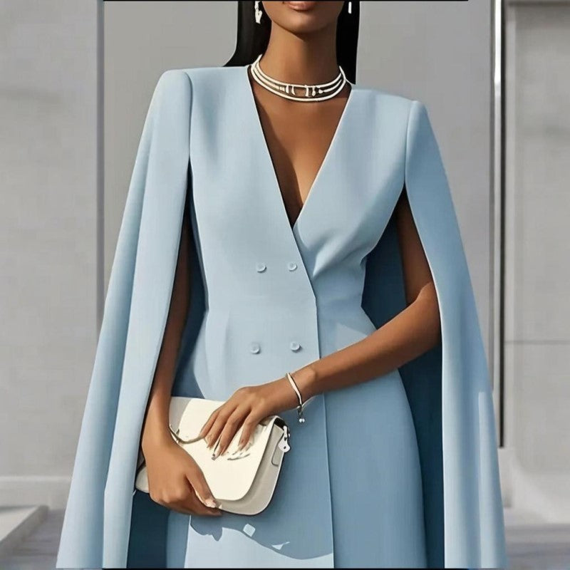 Woman wearing a light blue cape over a dress, holding a white handbag against a neutral background.