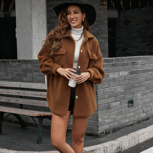 Woman in a brown coat and black hat holding a coffee cup on a city street.