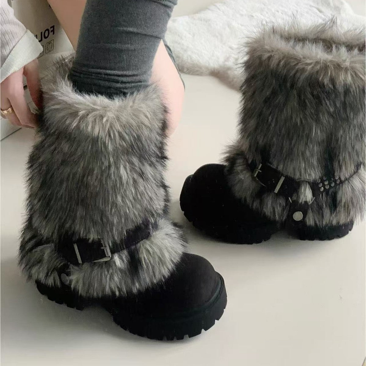 Black snow boots with gray fur trim worn by a person on a light background