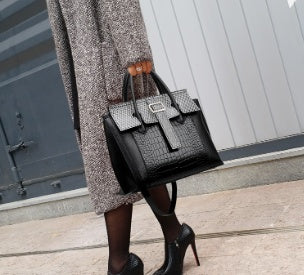 Person holding a black handbag with a textured pattern, wearing a coat and high heels.