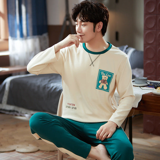 Person wearing a beige long-sleeve shirt with a teddy bear design and green pants sitting in a room.