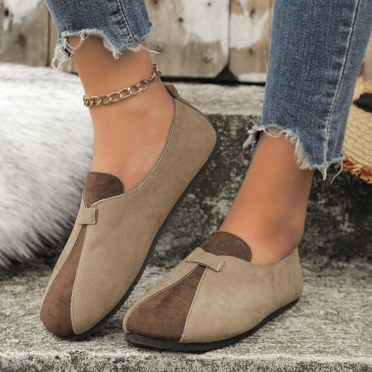 Pair of brown loafers worn with denim jeans on a textured surface.