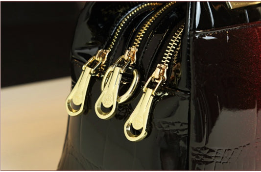 Black patent leather handbag with gold zippers on a blurred background
