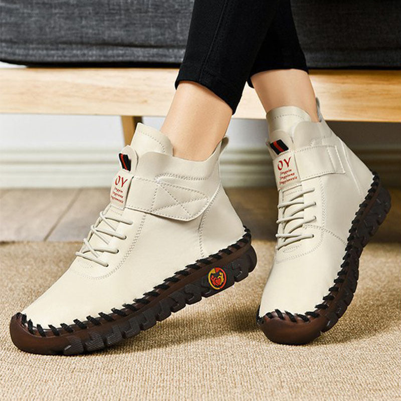 White ankle boots with brown soles worn by a person sitting on a couch.