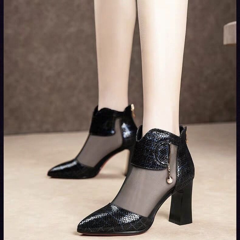 Black high-heeled shoes with mesh design worn by a person on a neutral background