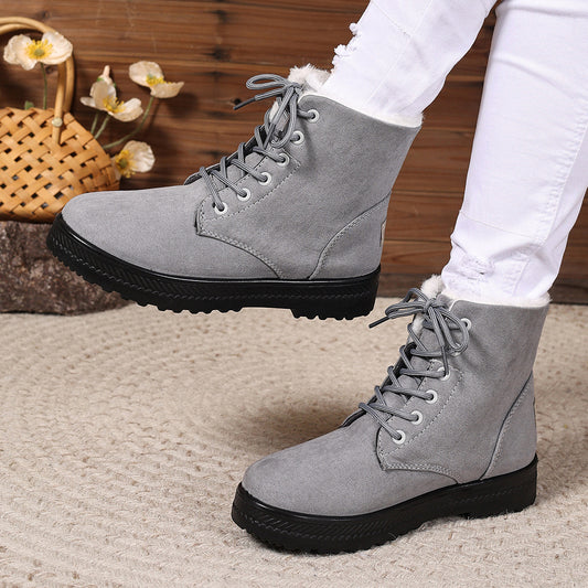 Gray lace-up boots with black soles worn by a person, with a blurred background.