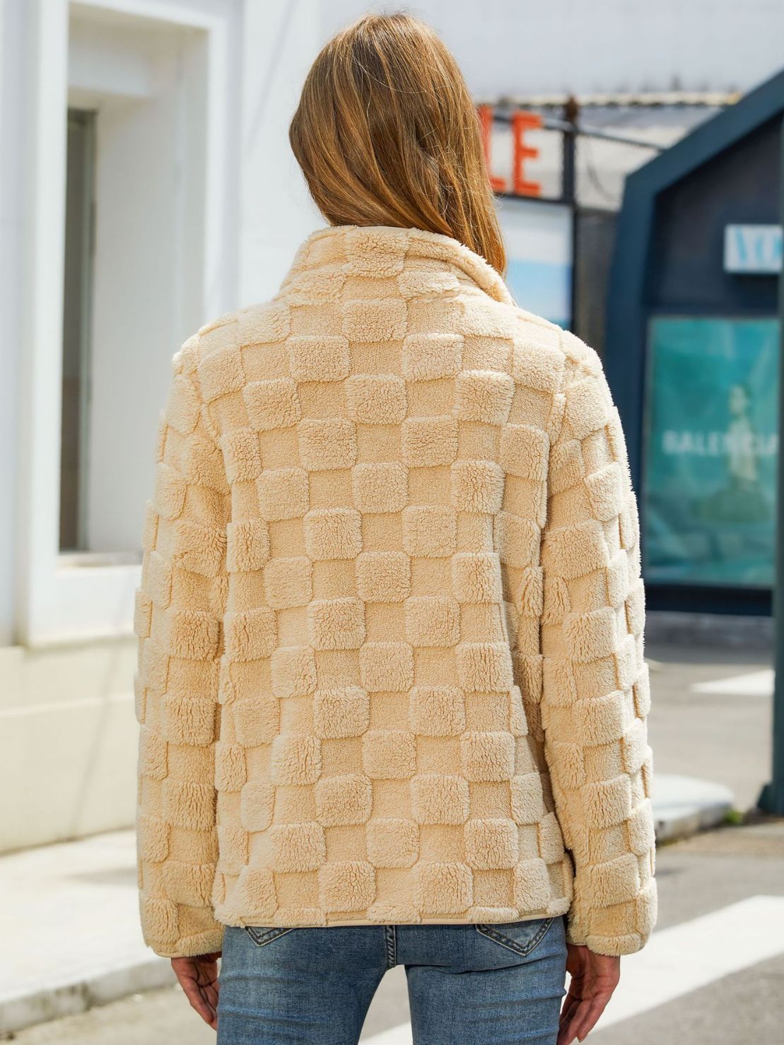 Person wearing a beige textured jacket outdoors with a blurred background
