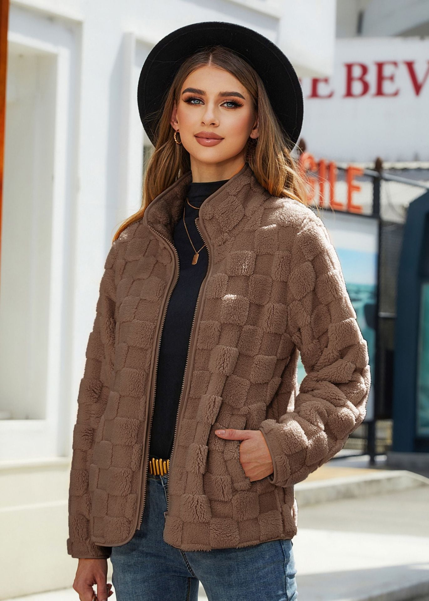 Woman wearing a brown quilted jacket and black hat outdoors.