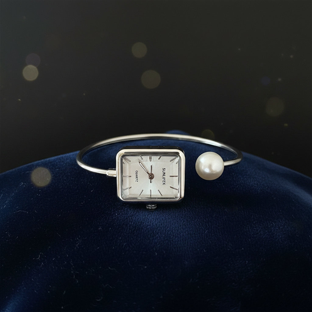 Silver bracelet with a square watch face and pearl accent on a gray fabric background