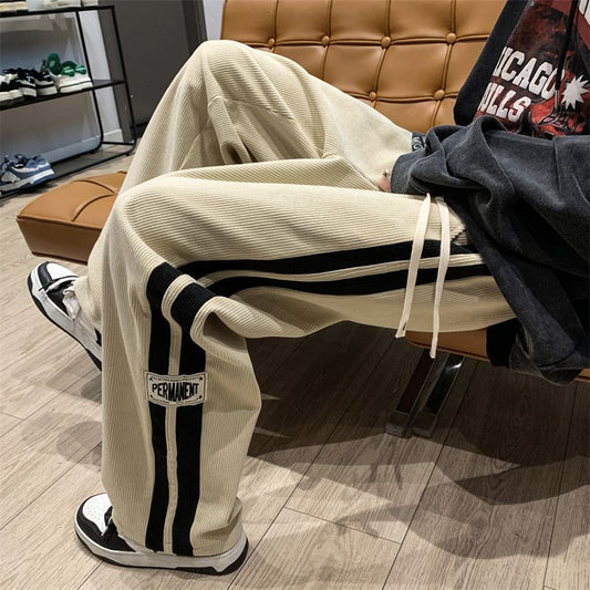 Person wearing beige corduroy pants with black stripes sitting on a brown leather chair.