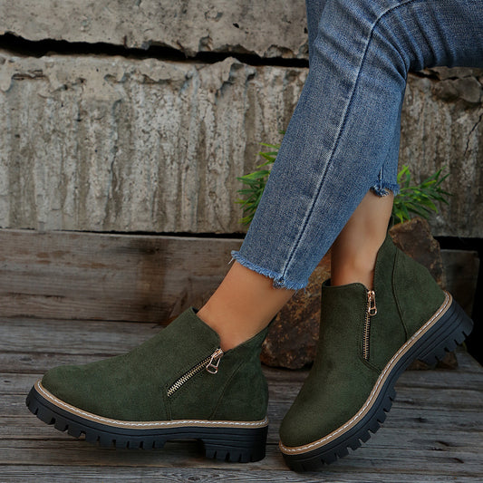 Green suede boots with zippers worn with blue jeans against a rustic background