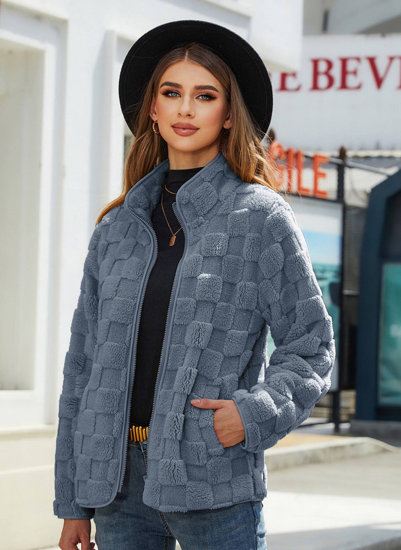 Woman wearing a textured blue jacket and black hat outdoors.