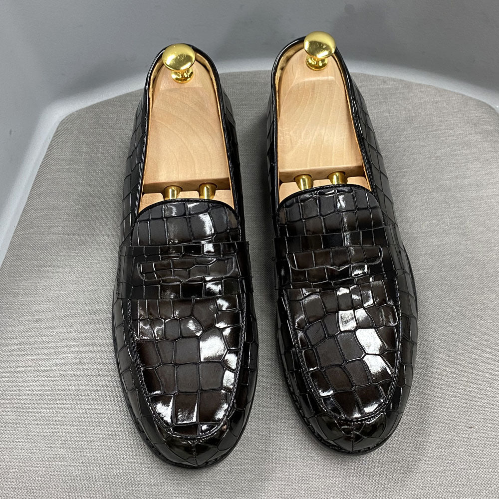 Black crocodile-patterned loafers with gold accents on a gray surface