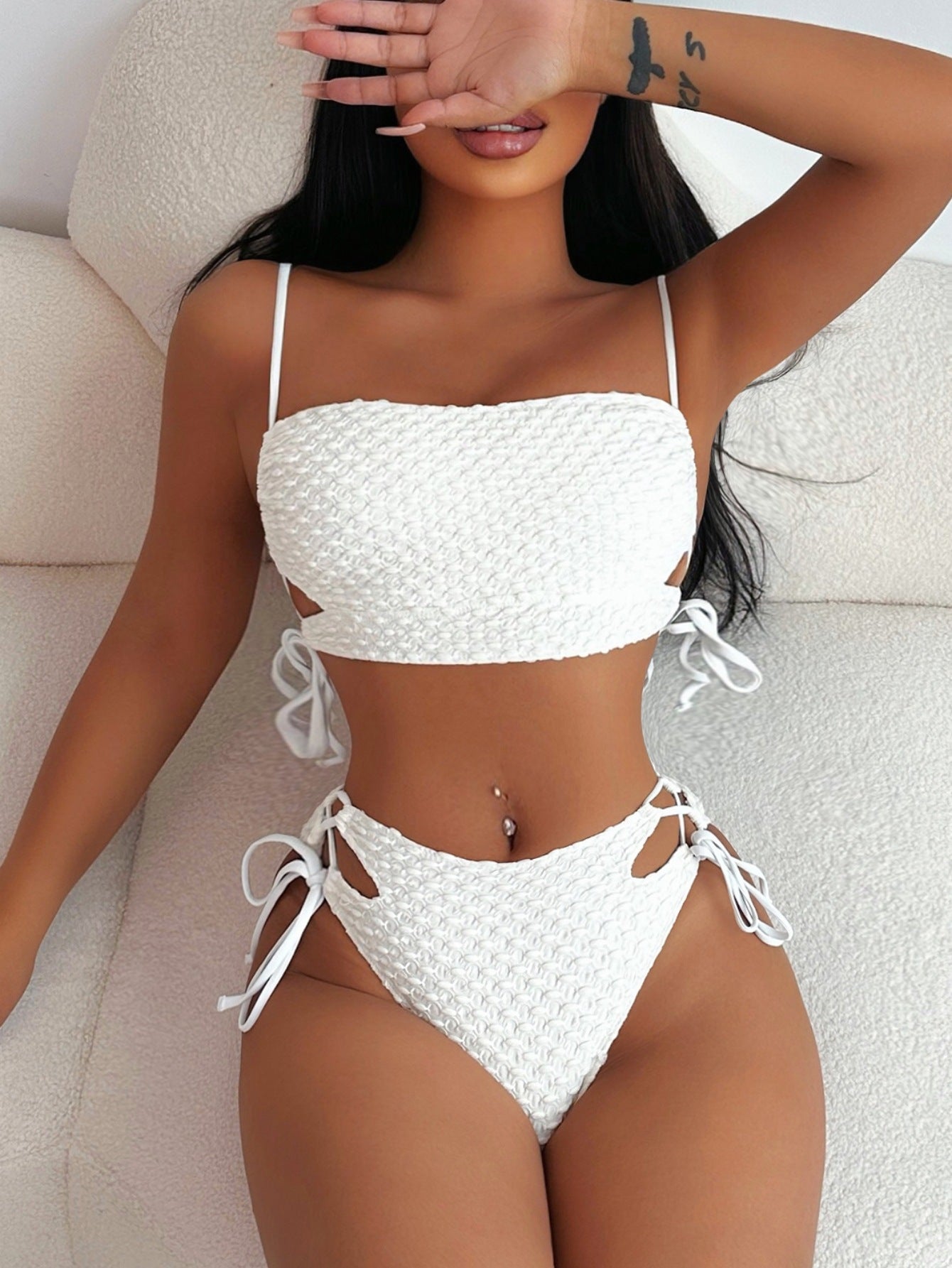 Woman wearing a white bikini sitting on a white couch.