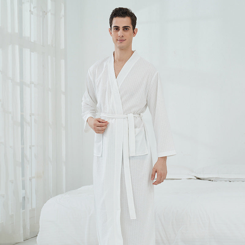 Man wearing a white robe standing in a bedroom with white curtains.