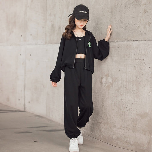 Person wearing a black outfit with a green ribbon, standing against a concrete wall.