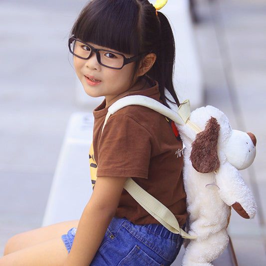 Young girl with glasses wearing a brown shirt and blue shorts, holding a plush dog toy.