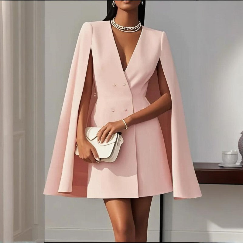 Woman wearing a pink cape dress holding a clutch in an indoor setting.