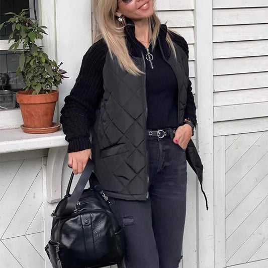 Woman wearing a black quilted vest and holding a black bag, standing in front of a white door.