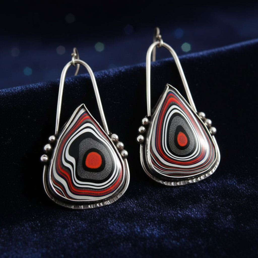 Teardrop-shaped earrings with Fordite stones on a stone background
