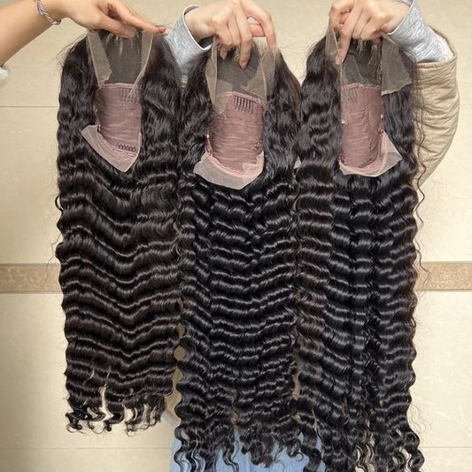 Three bundles of black hair extensions held by hands against a neutral background
