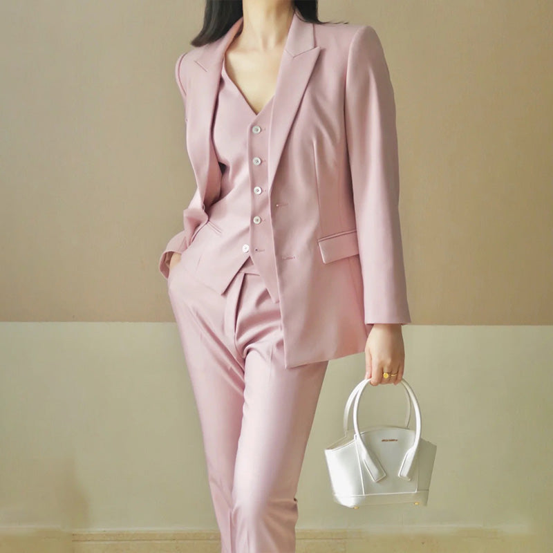 Person wearing a pink suit holding a white handbag against a plain background