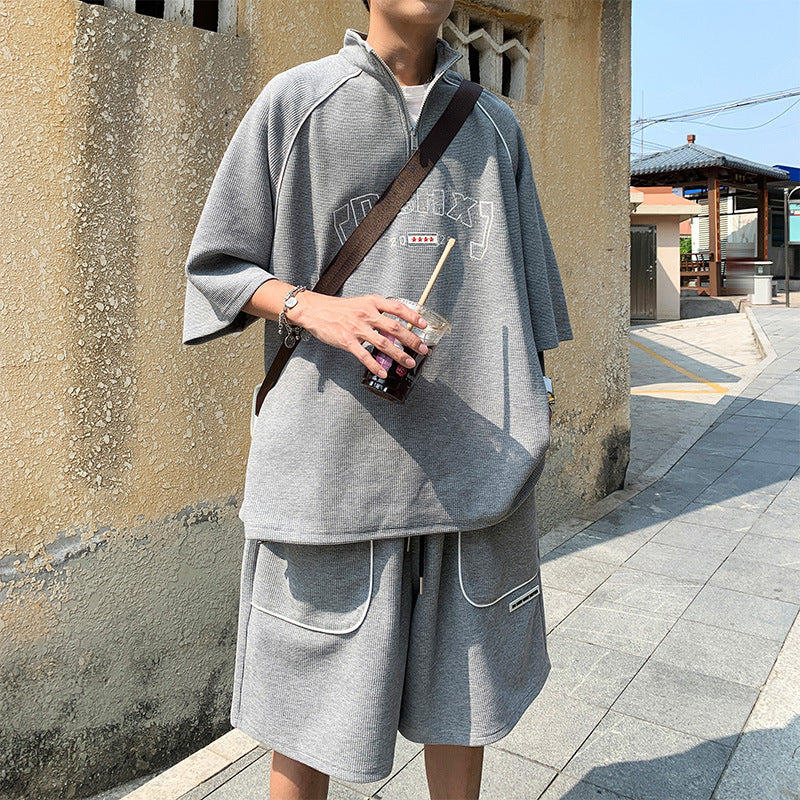 Person wearing a gray outfit with a crossbody bag, standing on a sidewalk.